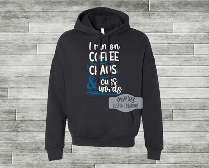 I Run on Coffee Chaos & Cuss Words black Bella+Canvas hoodie with white and sky blue HTV